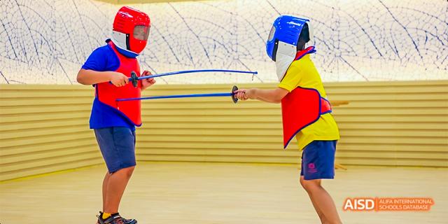 A student from Fettes College Guangzhou practicing fencing, wearing protective gear and holding a foil, with another student partially visible.