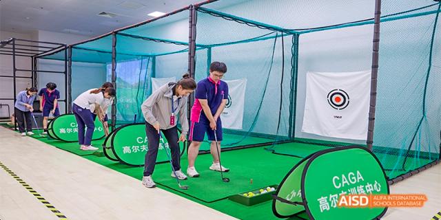 Two students at Fettes College Guangzhou practicing golf swing technique indoors at a golf simulator or driving bay.