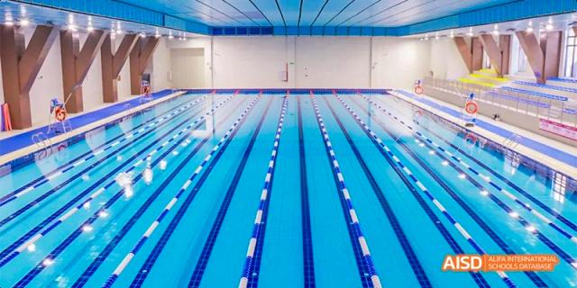 A wide-angle view of the empty, bright blue lanes and starting blocks of the indoor swimming pool at Fettes College Guangzhou.
