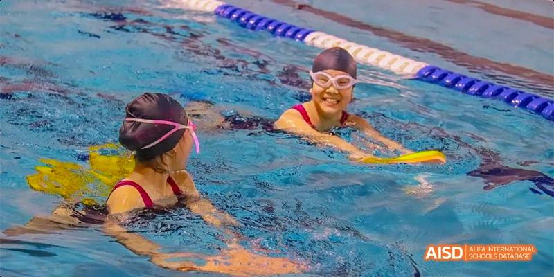 A smiling student from Fettes College Guangzhou, wearing swimming goggles, taking a lesson or participating in a water activity in the pool.