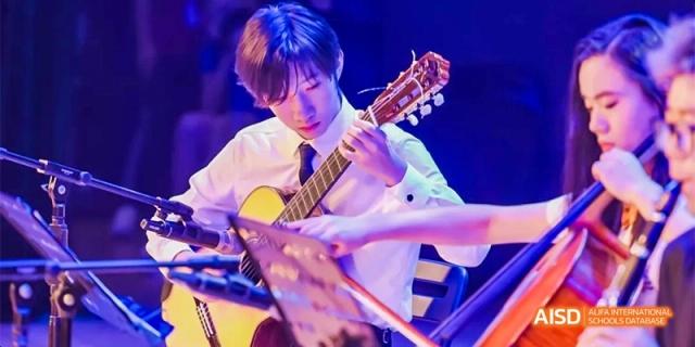 A close-up of a student from Fettes College Guangzhou playing a classical or acoustic guitar on a stage under vibrant blue lighting.