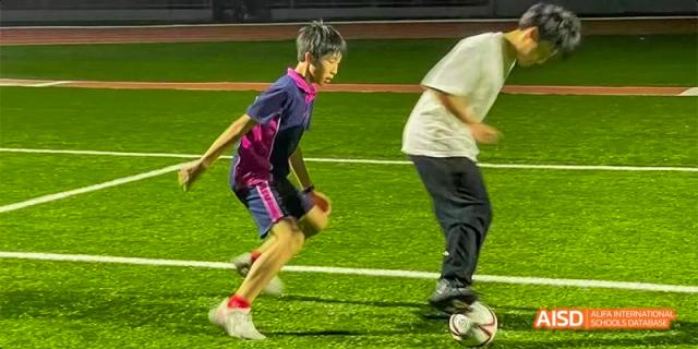 A close-up action shot of a student from Fettes College Guangzhou playing soccer on a green pitch, bending low to control the ball.