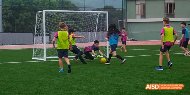 Students from Fettes College Guangzhou participating in a soccer practice, with several players focused on the ball near the goal net.