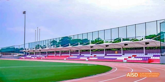 A wide view of the athletic facilities at Fettes College Guangzhou, showcasing a red running track and stadium seating under a bright sky.