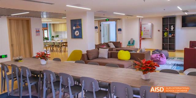A view of a bright student common room or cafeteria at Fettes College Guangzhou, featuring a long table and a comfortable lounge area with couches.