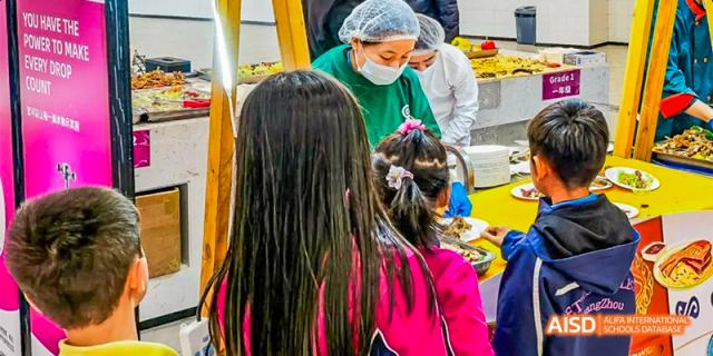 Two students at Fettes College Guangzhou interacting with a cafeteria or service worker who is wearing a mask and gloves.