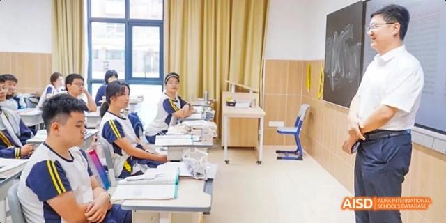 A Guangzhou Huamei International School student sitting alone at a desk in a well-lit classroom, focusing on their work.