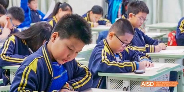 A young Guangzhou Huamei International School student intensely focused on writing notes or completing work at their desk.