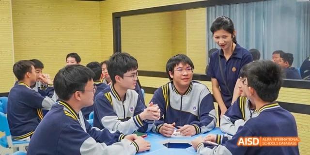 A group of Guangzhou Huamei International School students sitting around a blue table, smiling and engaged in a discussion or group activity.