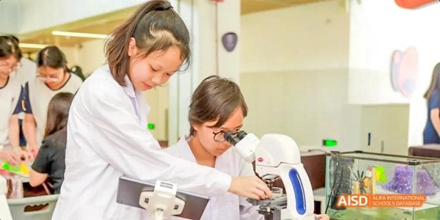 Two Guangzhou Huamei International School students collaborating on a science experiment, looking through a microscope in a lab.