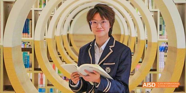 A Guangzhou Huamei International School student in uniform holding an open book and smiling, surrounded by a bright, modern, circular bookshelf structure.