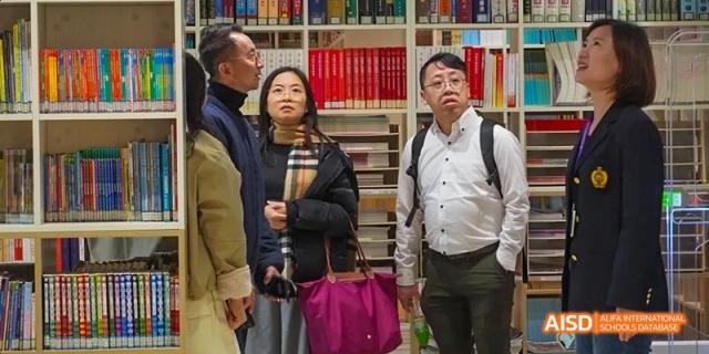 Guangzhou Huamei International School students and adults looking up with interest, surrounded by tall shelves of books in a library.