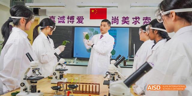 A teacher at Guangzhou Huamei International School in a lab coat holding a leaf and instructing students during a biology or chemistry class.