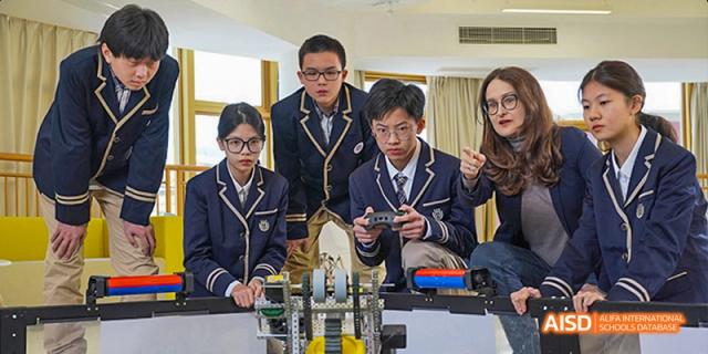 A group of Guangzhou Huamei International School students in uniform intensely focused on controlling a robotics or mechanical device.