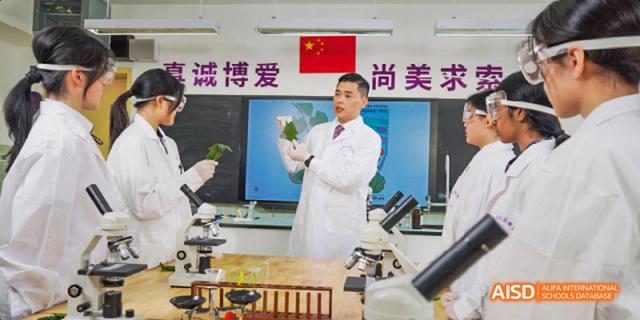 A Guangzhou Huamei International School teacher in a lab coat holding a leaf and instructing students during a science class.