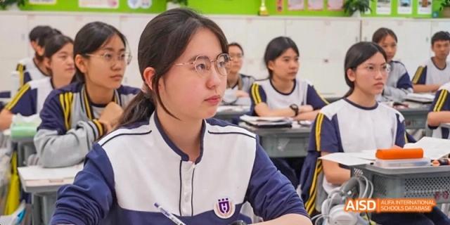 A Guangzhou Huamei International School student with glasses looking up attentively while sitting at a desk in a classroom.