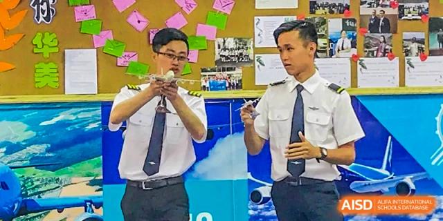 An aviation instructor and a Guangzhou Huamei International School student, both dressed in pilot-style shirts and ties, examining a small drone or model aircraft.