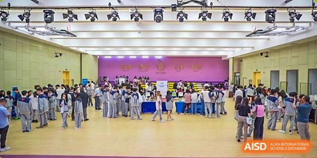 A large group of Guangzhou Huamei International School students in uniform gathered in a brightly lit auditorium or gymnasium.