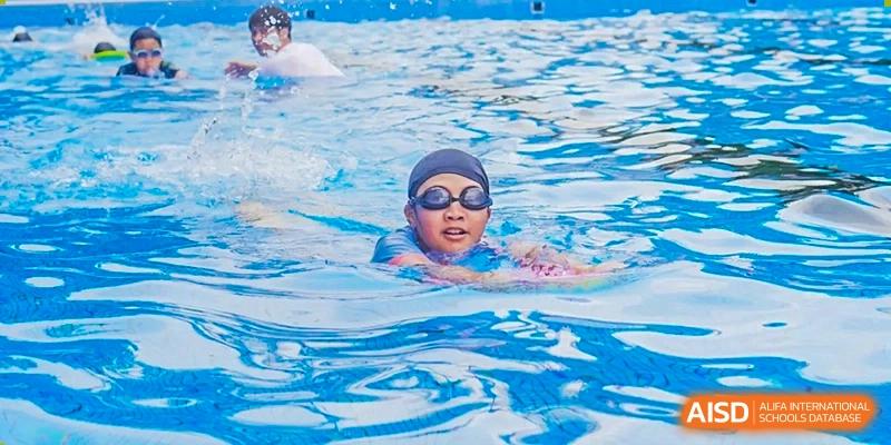 A young Guangzhou Huamei International School student wearing goggles and a swim cap, swimming laps in a pool.
