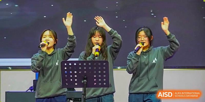 A Guangzhou Huamei International School student singing on stage with a microphone, hands raised, alongside a group of peers.