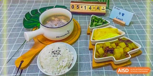 A healthy school meal set from Guangzhou Huamei International School featuring a bowl of soup, white rice, and side dishes of chopped vegetables.