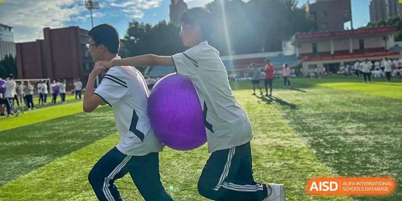 Two male students at Zhengzhou No.9 High School International Department work together to move or push a large purple ball during an outdoor sports activity.
