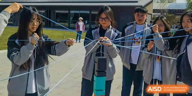 A female student at Zhengzhou No.9 High School International Department participates in a team-building exercise, using strings to carefully stack blocks on a platform.