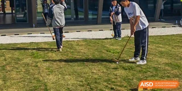 Zhengzhou No.9 High School International Department students standing outdoors on a lawn with a paved area in the background.