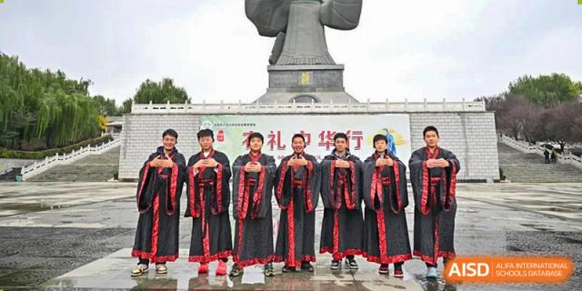 A group of Zhengzhou No.9 High School International Department students wearing traditional black and red outfits posing in front of a large statue.