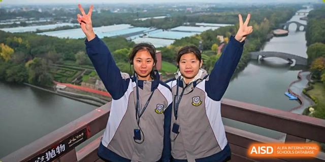 Two female students from Zhengzhou No.9 High School International Department raising their hands in excitement or victory outdoors.