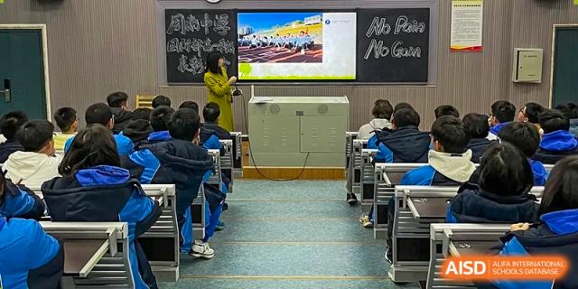 Students from Zhounan High School seated in a classroom facing a large projection screen and teaching equipment.