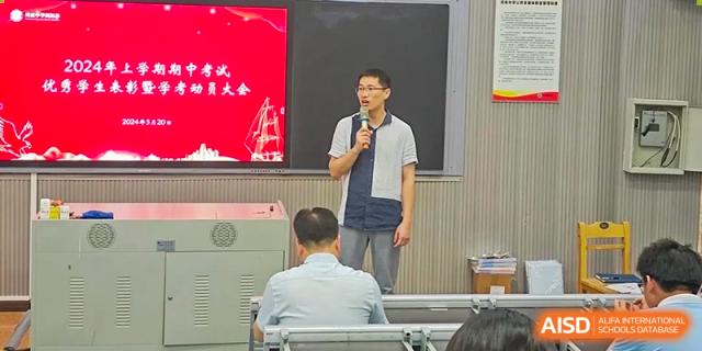 A teacher at Zhounan High School speaking to seated students in a classroom or small lecture hall.