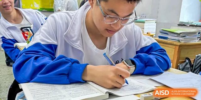 A male student from Zhounan High School wearing glasses and writing notes while studying at a desk.