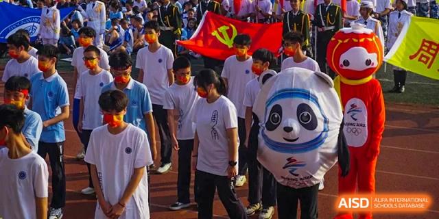 Zhounan High School students participating in a large outdoor gathering, with some holding a Chinese flag and a panda mascot.