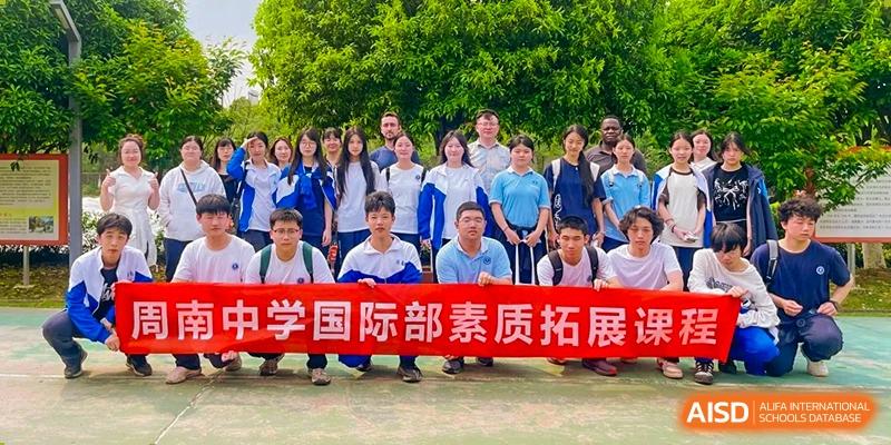 Group portrait of Zhounan High School students and teachers holding a red banner that reads "国际部素质拓展" (International Department Quality Development/Outreach).