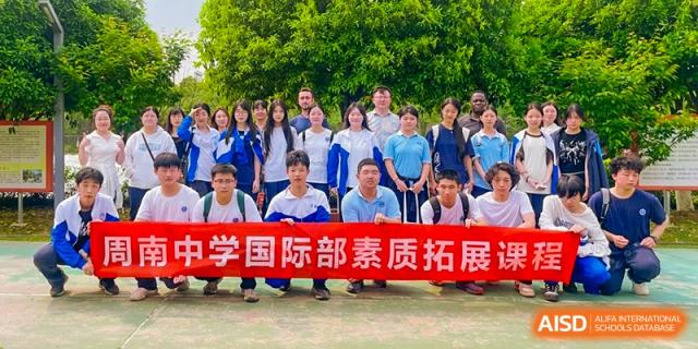 Group portrait of Zhounan High School students and teachers holding a red banner that reads "国际部素质拓展" (International Department Quality Development/Outreach).