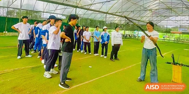 Zhounan High School students and a teacher standing in a line on an outdoor, covered green turf area for an activity.