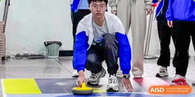A student from Zhounan High School playing a sport that appears to be curling or a similar activity on a hard surface.