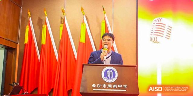 An administrator or guest speaking at a podium under the Chinese flag, likely at an event for Zhounan High School.