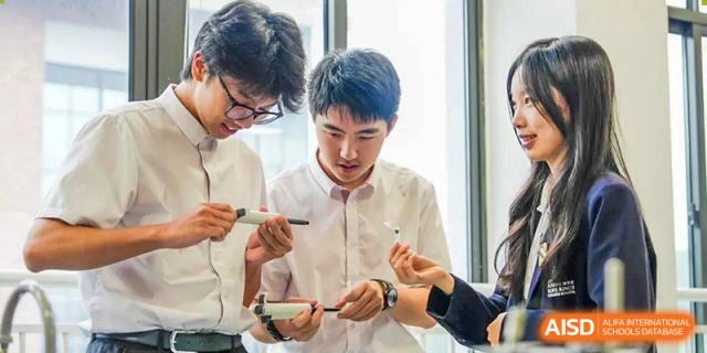 Students are working together on a project, looking at a small item. Hangzhou Dipont School of Arts and Science.