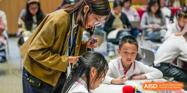 A student with long black hair is leaning over a table, engaged in a project. Hangzhou Dipont School of Arts and Science.