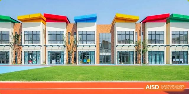 A modern school building with a red running track and a green lawn in front. Hangzhou Dipont School of Arts and Science.
