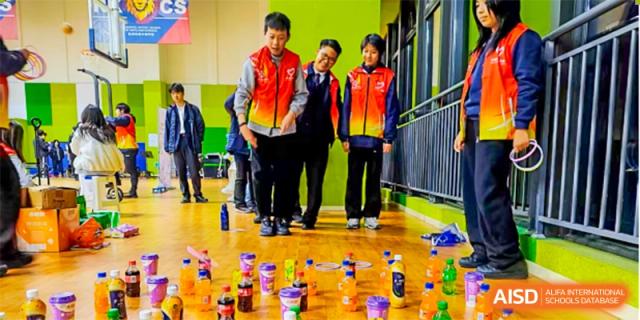 Students are engaged in a team building activity, standing around an assortment of bottles and cans on the floor. Hangzhou Dipont School of Arts and Science.