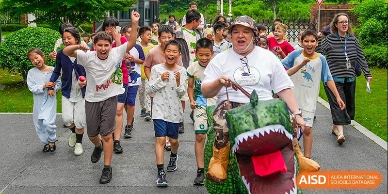 Young students are running during an outdoor event with a teacher in the lead. Hangzhou Dipont School of Arts and Science.