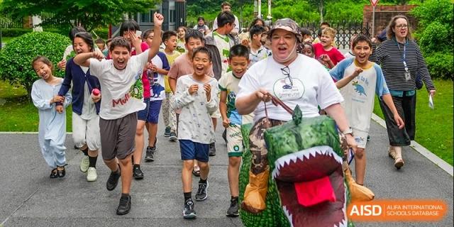 Young students are running during an outdoor event with a teacher in the lead. Hangzhou Dipont School of Arts and Science.