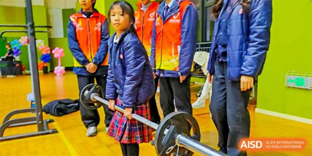A young female student in a blue jacket is standing next to a barbell. Hangzhou Dipont School of Arts and Science.