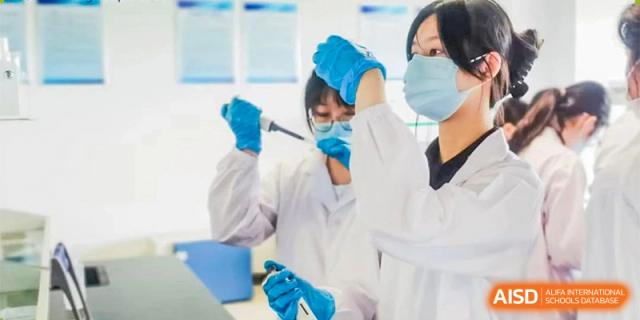 A student from Ningbo Huamao International School in a lab coat and gloves, performing a science experiment.
