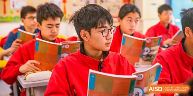 A student from Ningbo Huamao International School, wearing glasses and a red hoodie, taking notes in class.