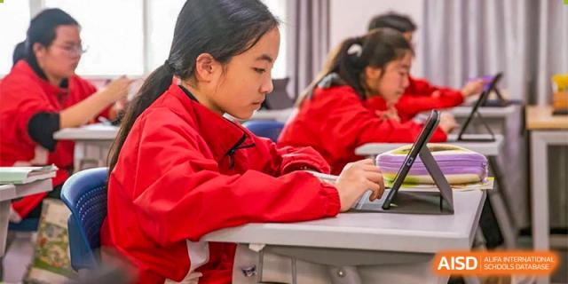 A student from Ningbo Huamao International School, in a red jacket, working on a laptop during class.