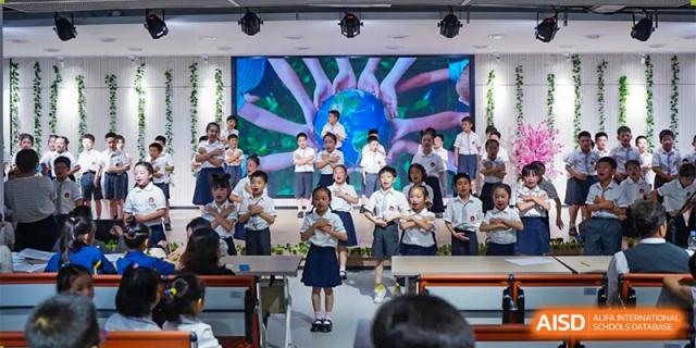 Ningbo Huamao International School students posing for a group photo on stage with a large screen behind them.